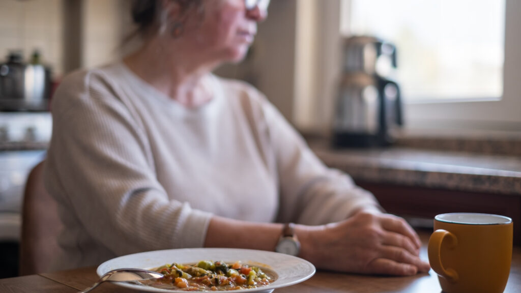Idosa sentada à mesa sem apetite