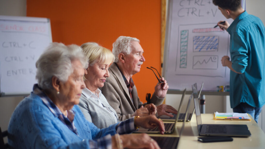 Idosos sentados numa sala a mexer em computadores