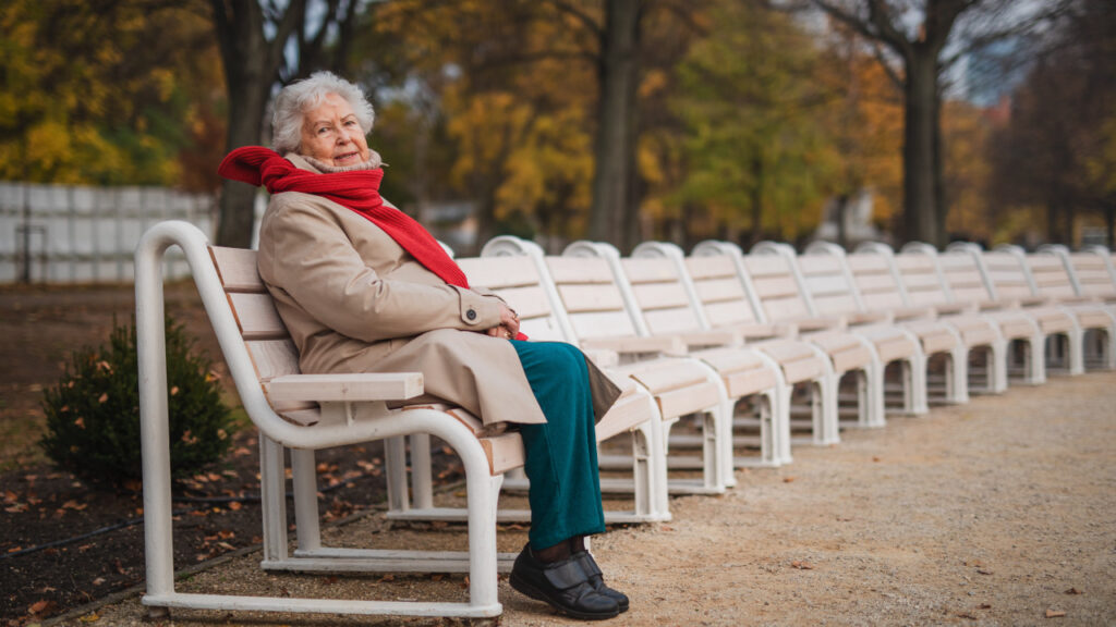 Idosa sentada num banco de jardim sozinha