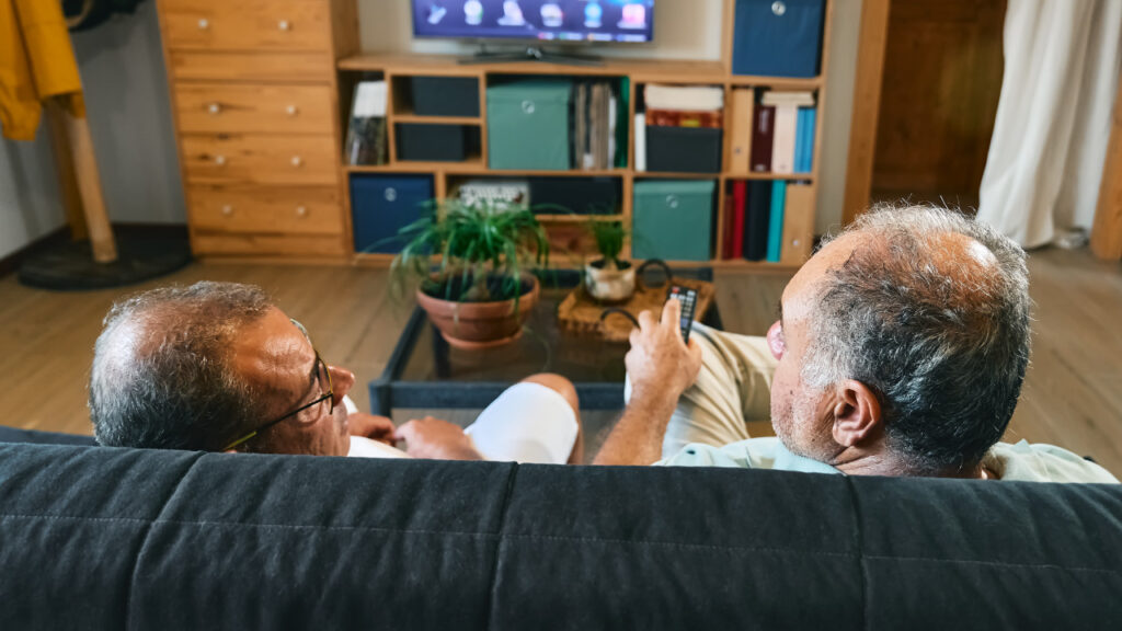 dois idosos sentados de frente para a televisão