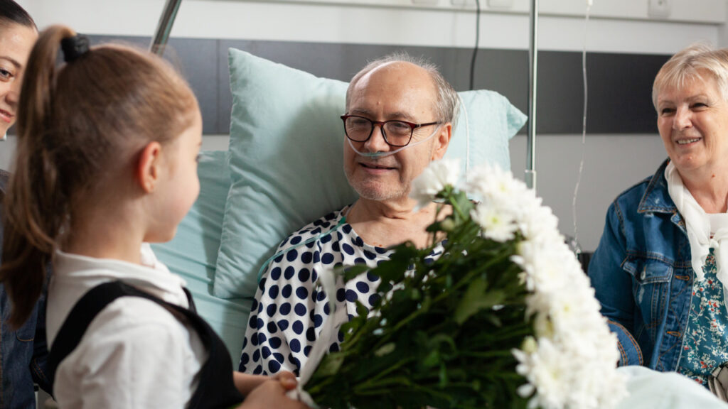 Idoso internado feliz rodeado da família e a receber flores da neta
