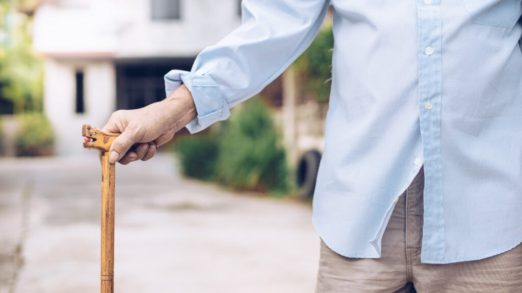 Idoso em pé no exterior da casa agarrado à sua bengala