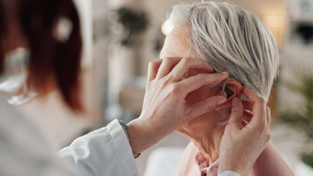Médica a colocar aparelho auditivos a uma idosa