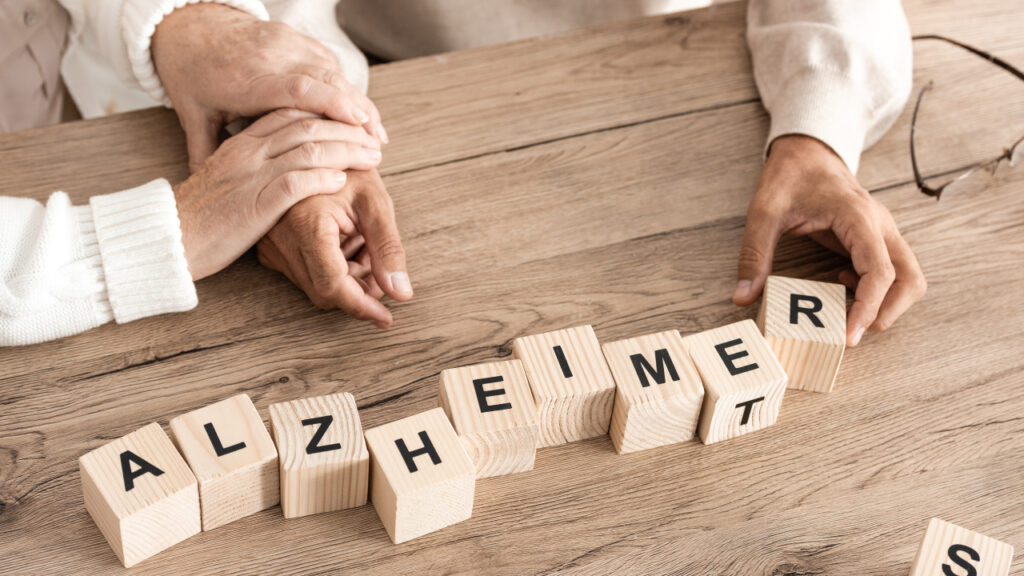 Senhor idoso a montar blocos com ajuda de cuidador e a escrever a palavra alzheimer